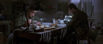 Movie still from “Patriot Games” (1992), directed by Phillip Noyce – Two men sitting at a dinner table eating sandwiches; Medium shot, Low angle