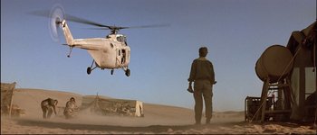 Movie still from “Patriot Games” (1992), directed by Phillip Noyce – A man standing in the sand looking at a helicopter; Wide shot, Low angle