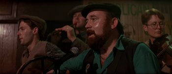 Movie still from “Patriot Games” (1992), directed by Phillip Noyce – A man with a beard is singing into a microphone; Close Up shot, Low angle