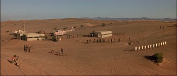 Movie still from “Patriot Games” (1992), directed by Phillip Noyce – A group of people standing around a helicopter in the desert; Extreme Wide shot, High angle