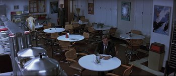Movie still from “Patriot Games” (1992), directed by Phillip Noyce – A man sitting at a table in front of two other men; Wide shot, High angle