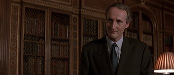 Movie still from “Patriot Games” (1992), directed by Phillip Noyce – A man in a suit standing in front of bookcases; Close Up shot, Low angle