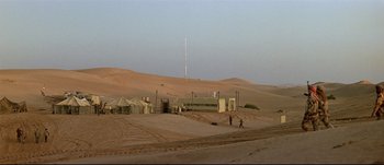 Movie still from “Patriot Games” (1992), directed by Phillip Noyce – A man walking across a dirt road in the desert; Extreme Wide shot, High angle