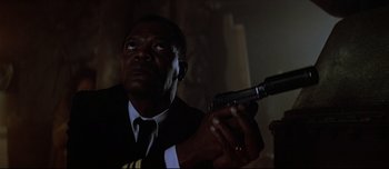 Movie still from “Patriot Games” (1992), directed by Phillip Noyce – A man in a suit and tie holding a gun in his hand; Close Up shot, Low angle