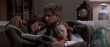 Movie still from “Patriot Games” (1992), directed by Phillip Noyce – A man and a woman and a little girl laying on a bed; Medium shot, High angle