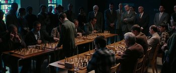 Movie still from “Pawn Sacrifice” (2014), directed by Edward Zwick – A group of people standing around a table with chess pieces on top of it; Wide shot, High angle