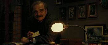 Movie still from “Pawn Sacrifice” (2014), directed by Edward Zwick – An older man sitting at a table with a lamp; Medium shot, Over the shoulder angle