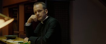 Movie still from “Pawn Sacrifice” (2014), directed by Edward Zwick – A man wearing a priest's outfit sitting at a table with his hand on his chin; Close Up shot, Low angle