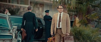 Movie still from “Pawn Sacrifice” (2014), directed by Edward Zwick – A man in a suit and tie holding a briefcase in front of two other men; Medium shot, Over the shoulder angle