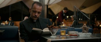 Movie still from “Pawn Sacrifice” (2014), directed by Edward Zwick – A priest is reading a book at a restaurant; Close Up shot, Low angle