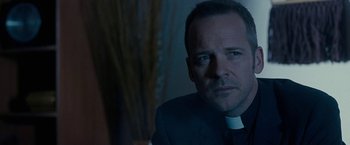 Movie still from “Pawn Sacrifice” (2014), directed by Edward Zwick – A man wearing a priest's outfit looking at the camera; Close Up shot, Over the shoulder angle