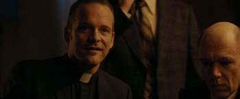 Movie still from “Pawn Sacrifice” (2014), directed by Edward Zwick – A man in a priest's outfit smiling for the camera; Close Up shot, Over the shoulder angle