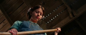 Movie still from “Pearl” (2022), directed by Ti West – A young girl holding a wooden stick in a room; Medium shot, Low angle