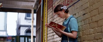 Movie still from “Pearl” (2022), directed by Ti West – A woman is reading a book outside of a building; Medium shot, Over the shoulder angle