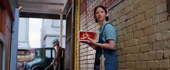 Movie still from “Pearl” (2022), directed by Ti West – A woman holding a box in front of a brick wall; Medium shot, Low angle