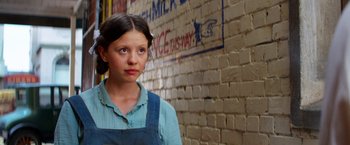 Movie still from “Pearl” (2022), directed by Ti West – A young girl standing in front of a brick wall; Close Up shot, Over the shoulder angle