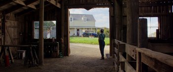 Movie still from “Pearl” (2022), directed by Ti West – A woman standing in a barn looking out at a house; Wide shot, Low angle