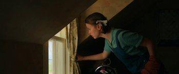 Movie still from “Pearl” (2022), directed by Ti West – A woman standing in front of a window with curtains; Medium shot, Low angle