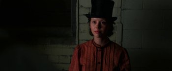 Movie still from “Pearl” (2022), directed by Ti West – A woman wearing a top hat in front of a brick wall; Close Up shot, Low angle
