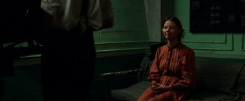 Movie still from “Pearl” (2022), directed by Ti West – A woman sitting on a bench in front of a wall; Medium shot, Over the shoulder angle