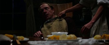 Movie still from “Pearl” (2022), directed by Ti West – A man sitting at a table with a knife in his mouth; Medium shot, Over the shoulder angle