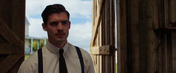 Movie still from “Pearl” (2022), directed by Ti West – A man wearing a tie standing in front of a wooden structure; Close Up shot, Low angle