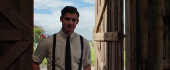 Movie still from “Pearl” (2022), directed by Ti West – A man wearing a tie standing in front of a barn door; Medium shot, Over the shoulder angle