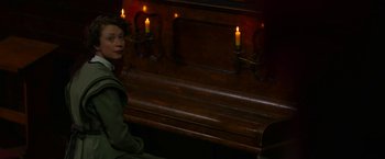 Movie still from “Pearl” (2022), directed by Ti West – A woman sitting in front of a wooden bench with lit candles on it; Medium shot, High angle