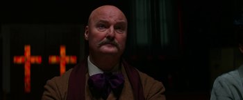 Movie still from “Pearl” (2022), directed by Ti West – A bald man with a mustache wearing a purple bow tie; Close Up shot, Low angle