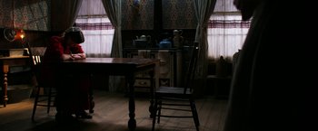 Movie still from “Pearl” (2022), directed by Ti West – An old wooden table and chair in a dark room; Wide shot, High angle