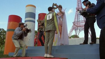 Movie still from “Pee-wee's Big Adventure” (1985), directed by Tim Burton – A man standing on a stage with a woman in front of a camera; Wide shot, Low angle