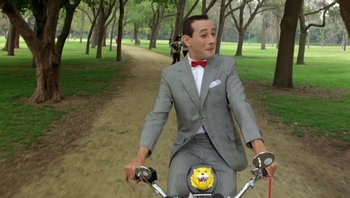 Movie still from “Pee-wee's Big Adventure” (1985), directed by Tim Burton – A man riding a bike down a dirt road; Wide shot, High angle