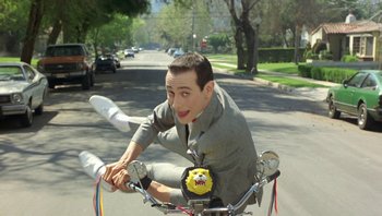 Movie still from “Pee-wee's Big Adventure” (1985), directed by Tim Burton – A man riding a bike down a street; Wide shot, Low angle