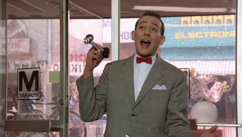 Movie still from “Pee-wee's Big Adventure” (1985), directed by Tim Burton – A man in a gray suit holding a microphone; Medium shot, Low angle