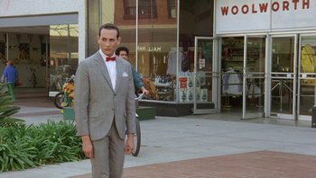 Movie still from “Pee-wee's Big Adventure” (1985), directed by Tim Burton – A man in a suit and bow tie standing on the sidewalk; Wide shot, Over the shoulder angle