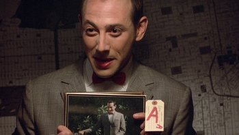 Movie still from “Pee-wee's Big Adventure” (1985), directed by Tim Burton – A man in a suit holding up a picture of himself; Close Up shot, Overhead angle