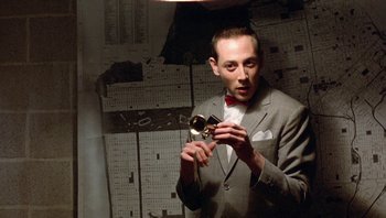 Movie still from “Pee-wee's Big Adventure” (1985), directed by Tim Burton – A man in a gray suit holding an object in his hand; Close Up shot, Overhead angle