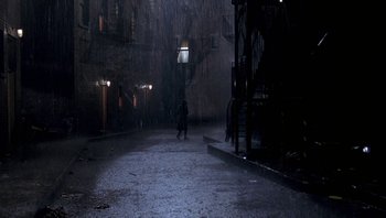 Movie still from “Pee-wee's Big Adventure” (1985), directed by Tim Burton – A person walking down a street in the rain; Extreme Wide shot, High angle