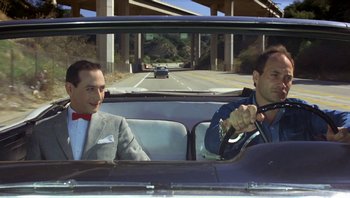 Movie still from “Pee-wee's Big Adventure” (1985), directed by Tim Burton – Two men in a car driving down a highway; Medium shot, Low angle