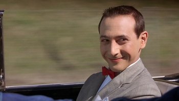 Movie still from “Pee-wee's Big Adventure” (1985), directed by Tim Burton – A man wearing a suit and a red bow tie sitting in the back of a car; Close Up shot, Low angle