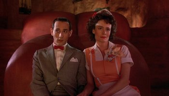 Movie still from “Pee-wee's Big Adventure” (1985), directed by Tim Burton – A man and a woman sitting next to each other on a couch; Medium shot, Low angle