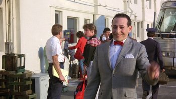 Movie still from “Pee-wee's Big Adventure” (1985), directed by Tim Burton – A man in a suit and bow tie standing in front of a group of people; Medium shot, Over the shoulder angle