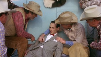 Movie still from “Pee-wee's Big Adventure” (1985), directed by Tim Burton – A man in a cowboy hat is sitting on the ground with two other men; Medium shot, High angle