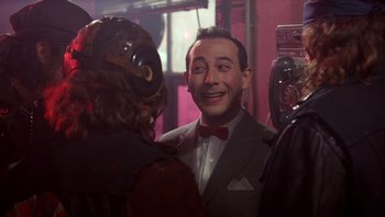 Movie still from “Pee-wee's Big Adventure” (1985), directed by Tim Burton – A man in a gray suit and red bow tie is smiling; Medium shot, Over the shoulder angle