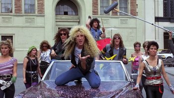 Movie still from “Pee-wee's Big Adventure” (1985), directed by Tim Burton – A group of people in a car with a car hood up; Medium shot, Low angle