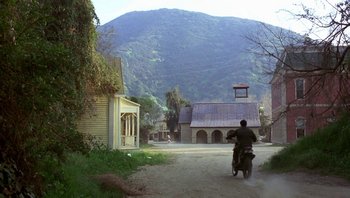 Movie still from “Pee-wee's Big Adventure” (1985), directed by Tim Burton – A man riding a motorcycle down a dirt road; Extreme Wide shot, Low angle