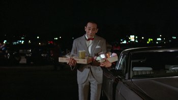 Movie still from “Pee-wee's Big Adventure” (1985), directed by Tim Burton – A man in a gray suit and red bow tie holding boxes of donuts; Medium shot, Over the shoulder angle