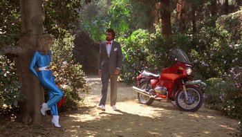 Movie still from “Pee-wee's Big Adventure” (1985), directed by Tim Burton – A man in a suit standing next to a red motorcycle; Wide shot, Low angle