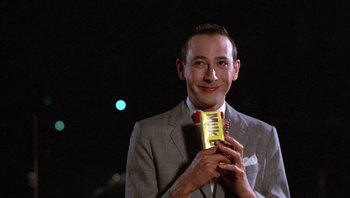 Movie still from “Pee-wee's Big Adventure” (1985), directed by Tim Burton – A man in a gray suit holding a chocolate bar in his hand; Close Up shot, Low angle