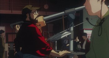 Movie still from “Perfect Blue” (1997), directed by Kô Matsuo – An animated man in a red shirt and brown hat is sitting at a desk; Medium shot, High angle